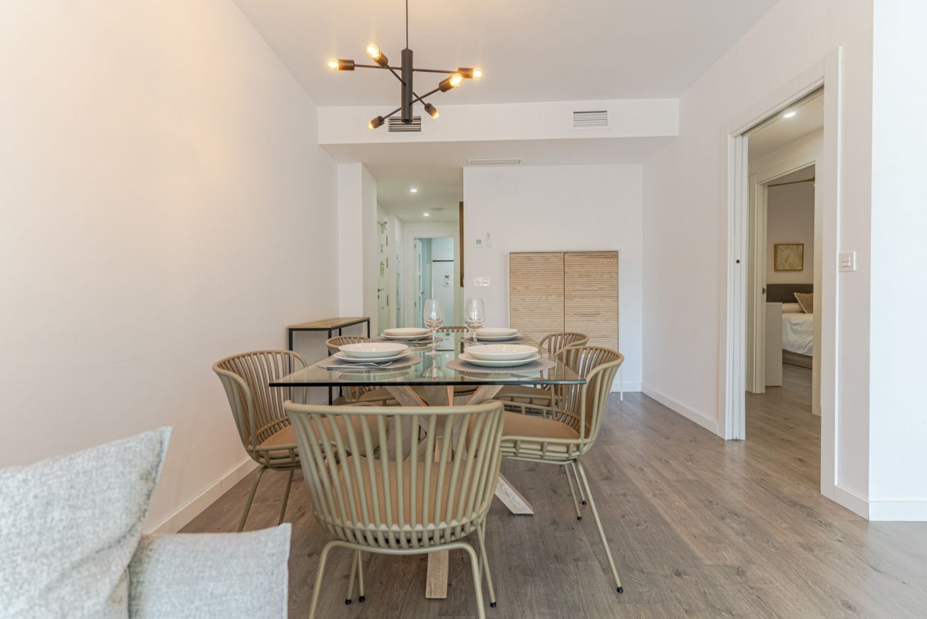 A dining area with a glass table, wicker chairs, and a modern pendant light.