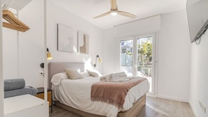 Une chambre à coucher comprenant un lit, des tables de chevet, un ventilateur de plafond et une porte-fenêtre coulissante donnant sur l’extérieur.