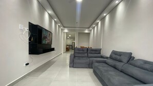 Ein modernes Wohnzimmer mit einem grauen Ecksofa, einem flachbildfernseher an der Wand und eingelassener Beleuchtung.