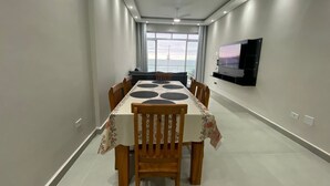 A modern dining area with a long table, chairs, a TV on the wall, and a view of the sea. - Apartment with sea view in Pitangueiras, incredible view, 1 parking space  (Centro Guarujá)