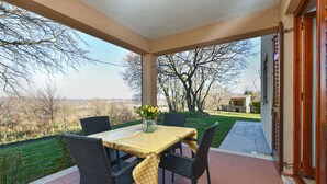 A covered patio with a table set for two, wicker chairs, and a view of a rural landscape. - Apartment 2372/141541 (Istria - Presika), 5000m from the beach (Presika)