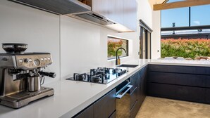 Une cuisine moderne équipée d’une machine à expresso Breville, d’une cuisinière à gaz et d’une grande fenêtre donnant sur un jardin.