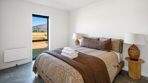 Une chambre à coucher avec un grand lit, deux lampes de chevet et une vue sur un paysage naturel, visible à travers une porte ouverte.