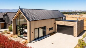 Une maison moderne dotée d’une grande baie vitrée, d’un garage et d’un toit en métal.