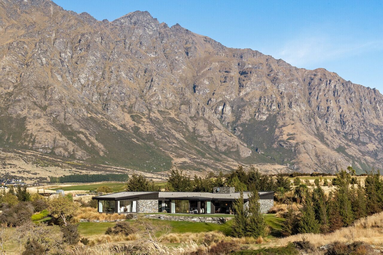 Una casa moderna con facciata in pietra, ampie finestre e vista su un paesaggio montuoso.