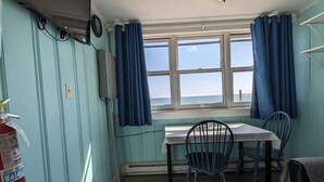 A room with a dining table and chairs, a fire extinguisher, a television mounted on the wall, and a window with curtains.