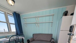 A compact room with a kitchenette, a sofa, a dining table with chairs, and a window with curtains.