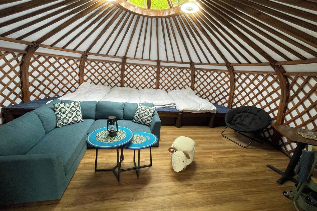 Ein Jurteninneres mit Bett, Sofa, kleinem Tisch und Stuhl.