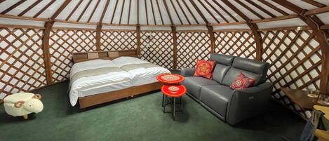 Interior de una yurta con cama, sofá y una pequeña mesa redonda.