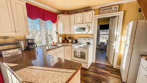 A kitchen with white cabinets, a granite countertop, a stove, a microwave, and a sign offering coffee for 5 cents daily. - New: Charming and Cozy, Great Value! (Swanton)