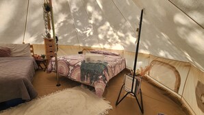 Una habitación con carpa, una cama, una mesita, una planta colgante y un letrero.