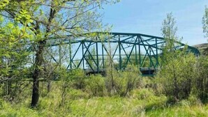 A steel bridge structure amidst a natural landscape with trees and grass. - #Y3 Willow Tree - 1 Queen bed - No Pets Please (Drumheller)