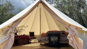 A tent with a "Welcome" mat, a bed, a table with a red and black checkered tablecloth, and a chair.