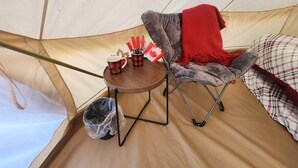 A tent interior with a foldable chair, a small round table with a mug and a flag, and a red blanket.