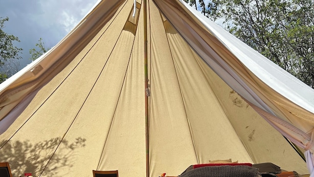 A tent with a "Welcome" mat, a sofa, a table with chairs, and a wood-burning stove.