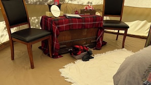 A cozy tent interior with two wooden chairs, a red plaid table, and a white rug.
