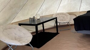 Interior de una carpa con una mesa, sillas y una cama.
