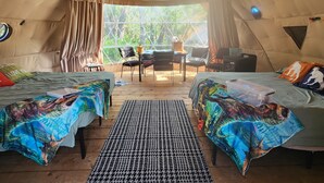 A cozy interior of a dome-shaped tent with two beds, a dining area, and a view of the outdoors.