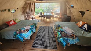 A cozy interior of a dome-shaped tent with two beds, a dining area, and a view of greenery outside.