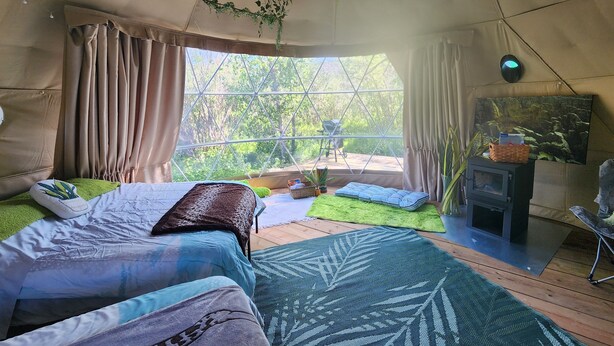 A cozy, well-lit tent-style room with a bed, a small fireplace, and a view of the outdoors. - #D3 Rainforest Getaway Dome- 2 Dbl beds-No pets Please (Drumheller)