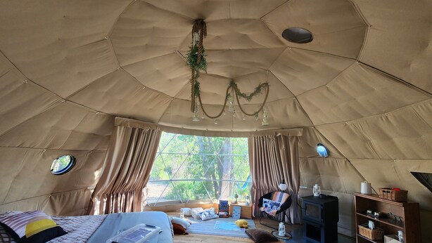 A cozy tented room with a bed, a small table, a chair, and a bookshelf. - #D4 Badlands Bunker Dome-1 Queen bed -Pet friendly (Drumheller)