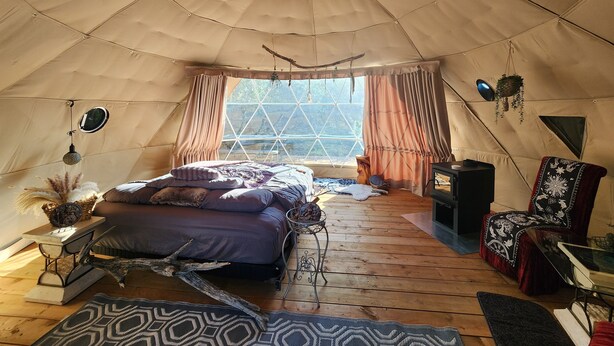 A cozy tented room with a bed, wooden flooring, a table, and a chair.