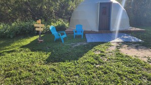 A dome-shaped yurt with a door and a small porch, two blue chairs, and a directional sign.