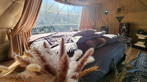 A cozy, well-lit tent with a large bed, curtains, and a view of the outdoors.