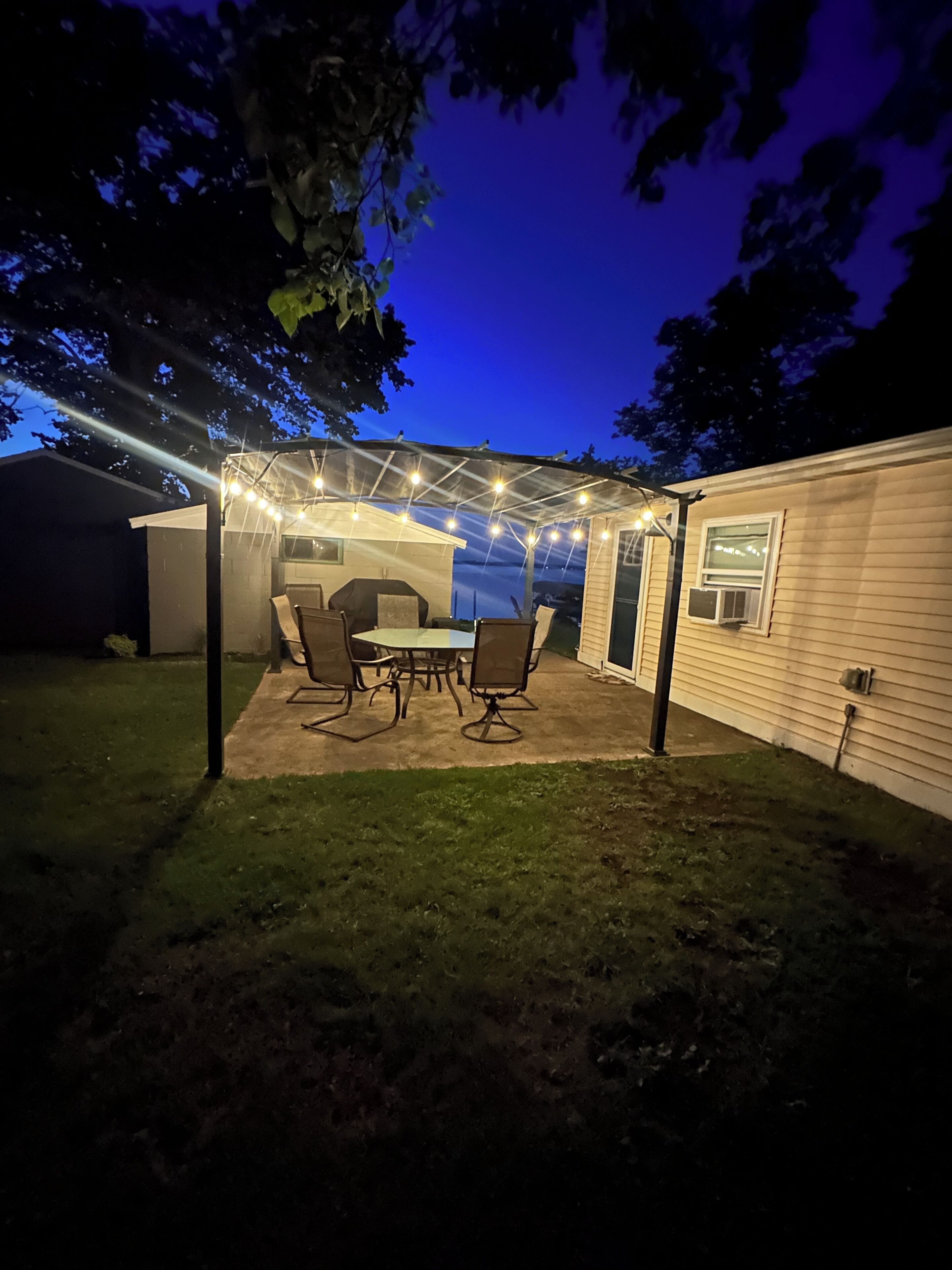 A covered patio with a table and chairs, a grill, and string lights.