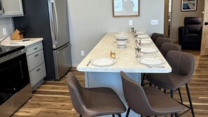 A modern kitchen with a central island, bar stools, and a dining table set for six. - Charming 3-bedroom cabin right on the sandy shore of beautiful Star Lake. (Dent)