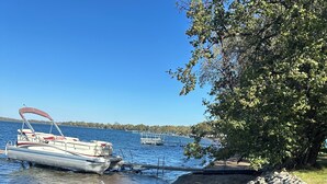 A lakeside scene with a boat docked near a rocky shoreline. - Charming 3-bedroom cabin right on the sandy shore of beautiful Star Lake. (Dent)