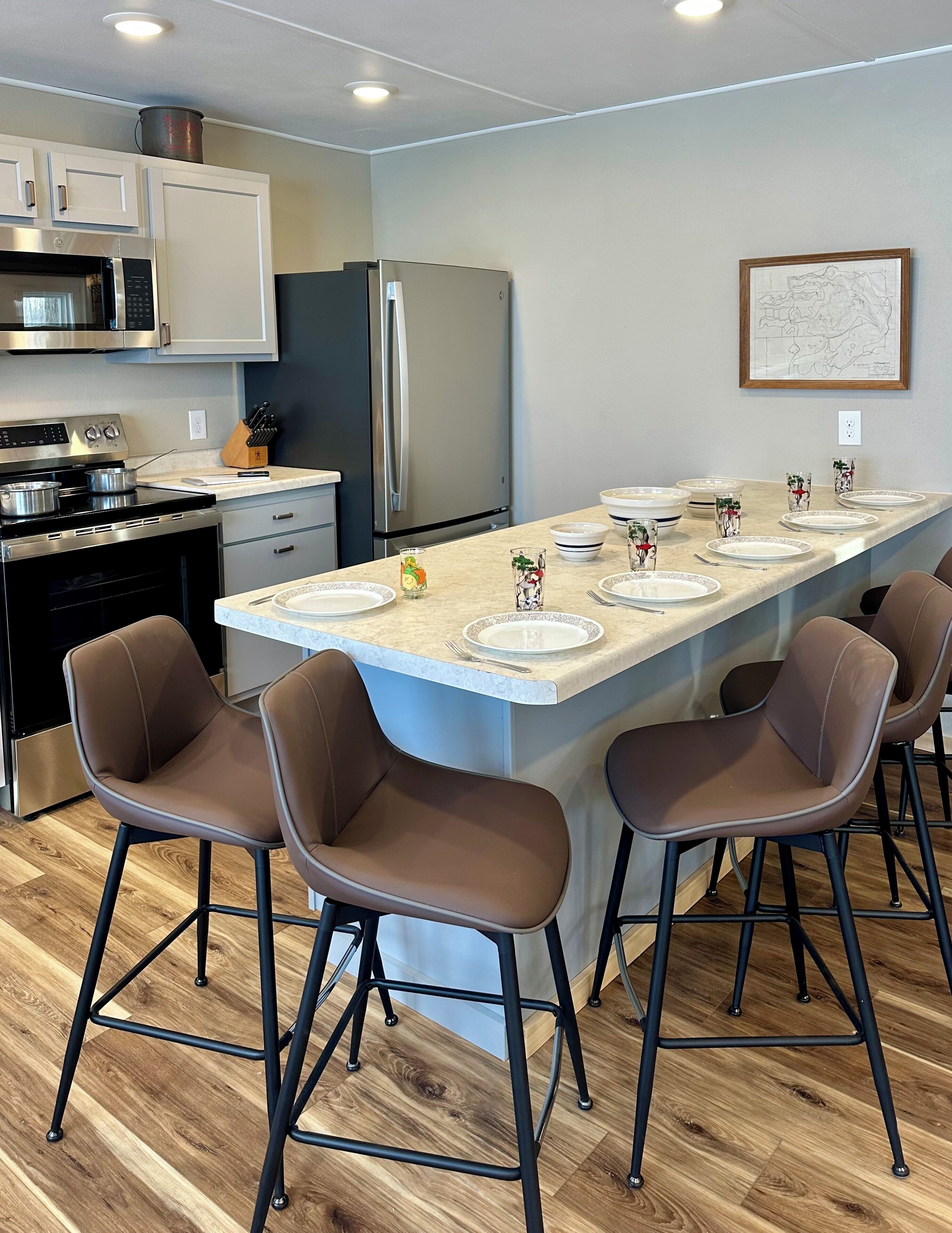 Une cuisine moderne dotée d’un îlot central, de tabourets de bar, d’appareils électroménagers en acier inoxydable et d’un coin repas aménagé pour quatre personnes.