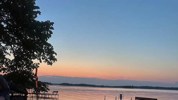 A lakeside view with a fire pit, benches, and a dock extending into the water. - Charming 3-bedroom cabin right on the sandy shore of beautiful Star Lake. (Dent)