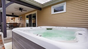 Un bain à remous situé dans un espace extérieur abrité, doté d’un ventilateur de plafond, d’une fenêtre et d’une terrasse avec des chaises et des tables.