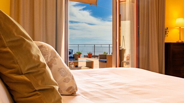 A hotel room with a bed, a balcony with outdoor furniture, and a view of the sea. - Open Horizon - Short Rent (Zafferana Etnea)