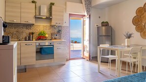 A modern kitchen with a built-in oven, a dining area with a table and chairs, and a view of the outdoors through an open door. - Open Horizon - Short Rent (Zafferana Etnea)