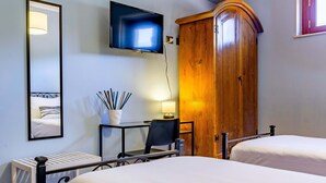 A hotel room with two beds, a TV mounted on the wall, a wooden wardrobe, a desk with a chair, and a bedside table with a lamp. - Open Horizon - Short Rent (Zafferana Etnea)
