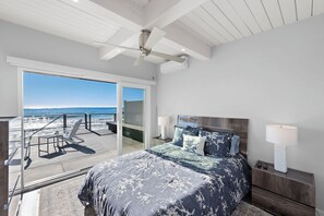 A bedroom with a large bed, a ceiling fan, and a view of the beach through a sliding door. - Oceanfront Retreat: 2BR Home with Private Beach Access, Firepit  
STR24-0040 (Dana Point)