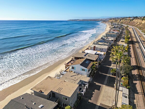 Zona residencial costera con casas junto a la playa y una vía de tren.