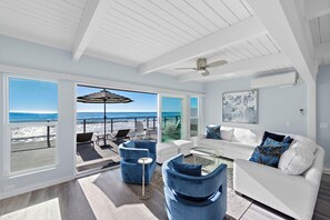 Amplia sala de estar con vista a la playa, muebles blancos y un ventilador de techo.