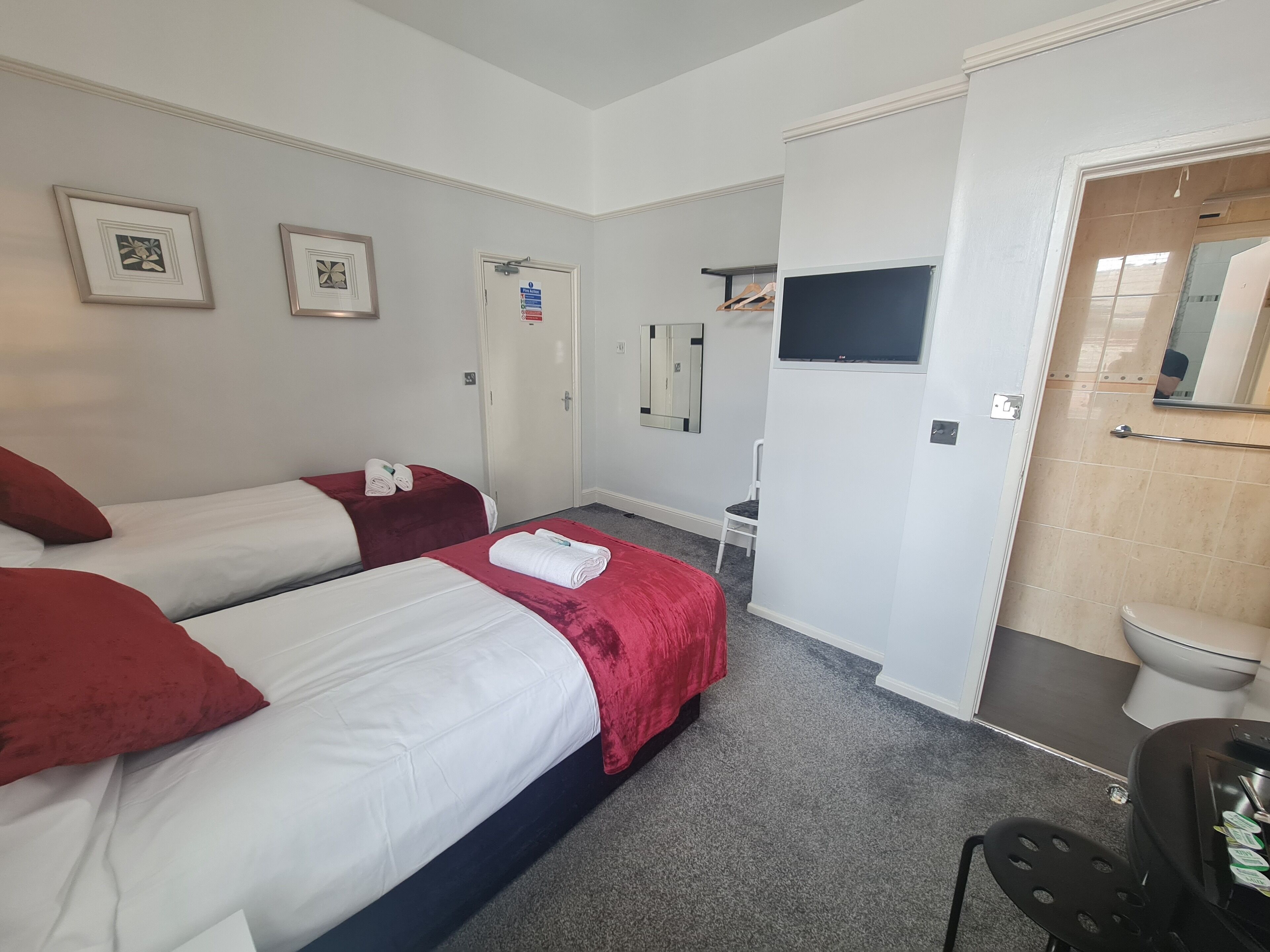Quarto de hotel com duas camas, uma pequena mesa, uma cadeira, televisão e banheiro visível através de uma porta aberta.