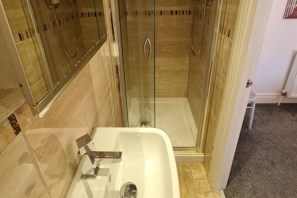 Un baño moderno con ducha de vidrio, un lavabo blanco y dos toallas blancas colgadas en la pared.