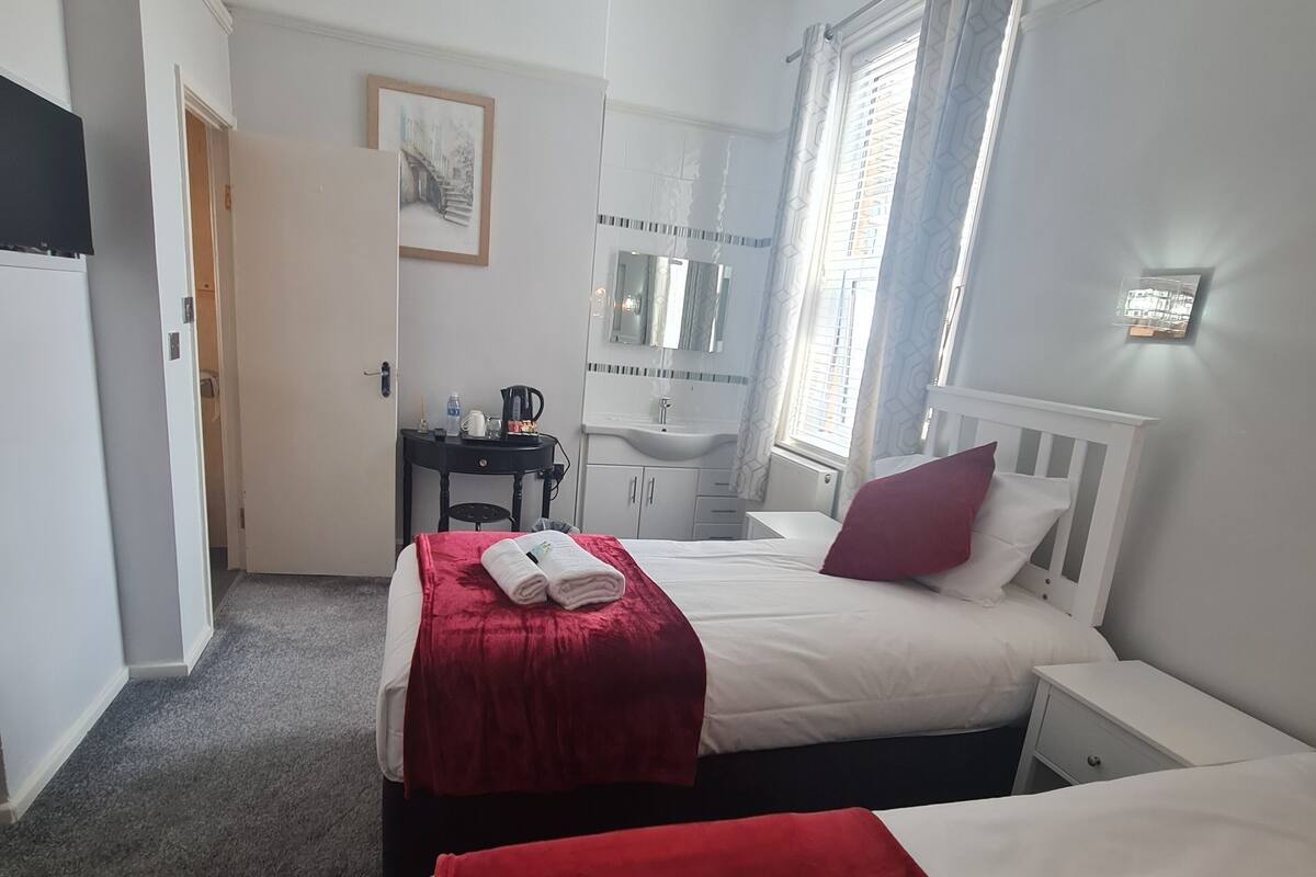 Habitación de hotel con dos camas, un escritorio, un baño y una puerta que da a otra habitación.