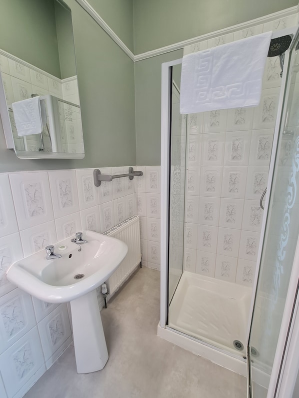 Un baño con lavamanos blanco, cabina de ducha de vidrio y espejo sobre el lavamanos.