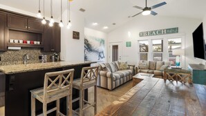 A modern kitchen with a granite countertop, wooden bar stools, a large island, and a ceiling fan. - Special Shell features 2BD/2BA w/private, fenced yard, swim spa, outdoor fireplace! (Port St. Joe)