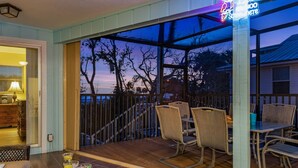 An outdoor patio with wicker furniture and a neon sign, overlooking a residential area.