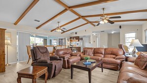 A spacious living room with leather sofas, wooden beams, ceiling fans, and a view to the outside.