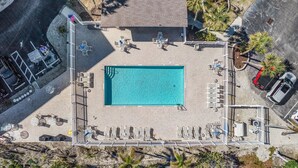 Luftaufnahme eines Poolbereichs mit rechteckigem Schwimmbecken, Liegestühlen und einer überdachten Sitzgelegenheit.