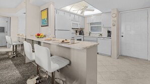 Eine moderne Küche mit wei ßen Schränken, einer zentralen Kochinsel mit Barhocker sowie Deckenventilator und Einbauleuchten.