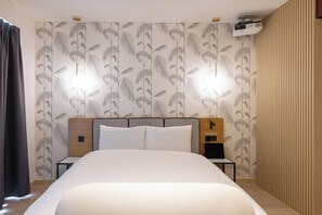 A hotel room with a large bed, a wooden headboard, a nightstand with a lamp, and a wall-mounted projector. - Brown-dot Hotel Haeundae (Busan)